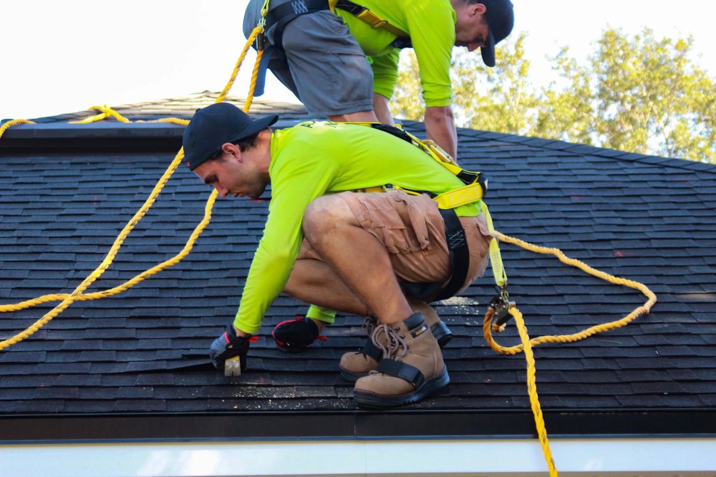 Two roofers installing shingles on a residential roof with safety harnesses
